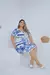 Modelo usando um vestido plus size branco com estampa azul, sentado em uma superfície clara.