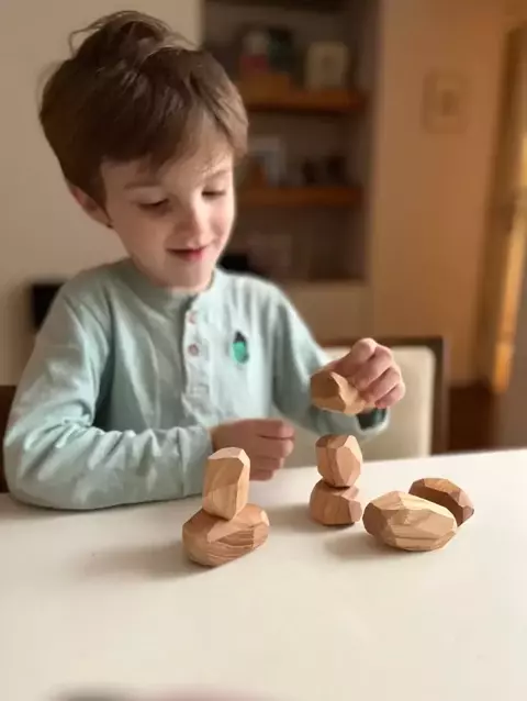 Niño jugando con piedras de equilibrio de madera sobre una mesa.