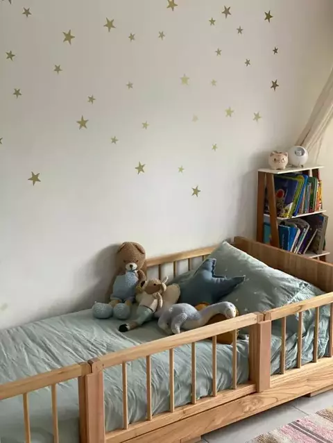 Cama infantil con muñecos de peluche y estrellas doradas en la pared.