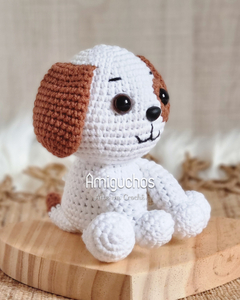 Boneco de crochê de um cachorrinho kawaii, com orelhas marrons e corpo branco, sentado sobre uma base de madeira.