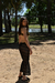 Modelo luciendo un bikini olivo con una falda de red negra en un entorno natural al aire libre.