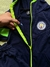 Conjunto deportivo color azul y verde flúor de Manchester City, mostrando la cremallera y el logo del club.