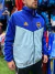 Campera rompeviento de Boca Juniors en azul y verde agua, modelo de Adidas, vista frontal de un hombre que la lleva puesta.