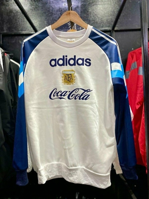 Buzo retro de Argentina 1996 en color blanco con detalles en azul y el logo de Adidas y Coca-Cola.