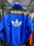 Chaqueta rompeviento retro de Adidas, color azul con detalles en negro y logo en la espalda.