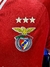 Escudo del Benfica con tres estrellas doradas en una camiseta roja.