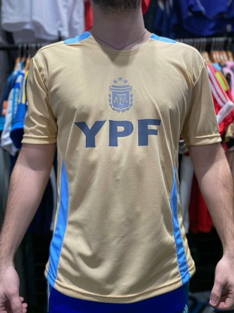 Camisa de fútbol color dorado con detalles en azul y el logo de la AFA, con la inscripción YPF en el frente.