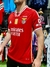 Camiseta roja del Benfica con detalles en blanco y el logo de Emirates, exhibida por un modelo en una tienda.