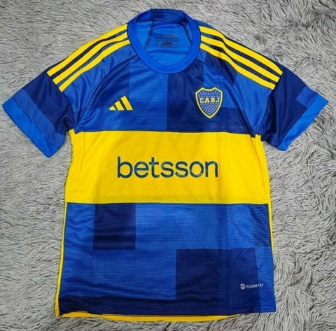 Camiseta titular de Boca Juniors 2024, con diseño en azul y amarillo, logotipo de la institución y patrocinador en el frente.