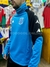 Buzo polera de Racing en color azul con detalles en negro y logo del club, exhibido en una tienda de ropa deportiva.