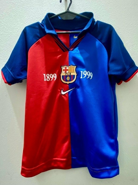 Camiseta retro de fútbol del FC Barcelona, diseño dividido en rojo y azul, con el escudo del club y las fechas 1899 y 1999.