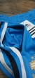 Pantalón de Argentina celeste rústico, con detalles en negro y blanco, mostrando el cierre y la etiqueta de la marca Adidas.