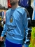 Buzo retro de Reebok en color celeste, con logo de la AFA y Coca-Cola, lucido por un modelo en una tienda de ropa deportiva.