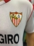 Detalle del escudo del Sevilla FC en la camiseta titular de Montiel, con franjas rojas y blancas.