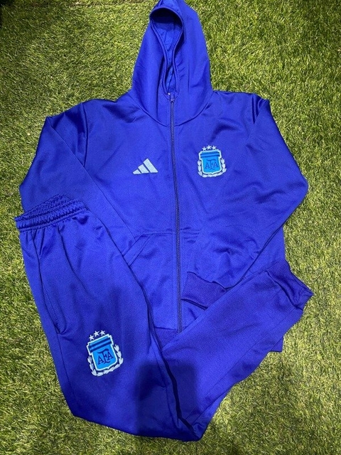 Conjunto deportivo azul para niño, compuesto por una campera con capucha y pantalones, con el logo de la AFA y detalles de Adidas.