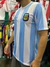 Camiseta titular de la selección argentina, modelo Maradona 1986, con franjas celestes y blancas y el escudo de la AFA.