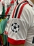 Camiseta blanca de fútbol con detalles rojos y negros, mostrando el logo de la UEFA en la manga.