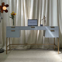 Escritorio moderno con cajones, florero con flores, computadora portátil y figura decorativa sobre fondo de cortinas claras.