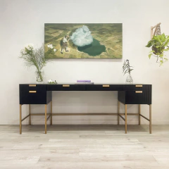 Un mueble negro con patas doradas decorado con flores y un cuadro surrealista en la pared que muestra un hombre y una nube sobre un paisaje agrícola.
