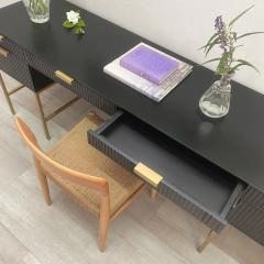 Vista superior de un escritorio negro con detalles dorados, una silla de mimbre y libros apilados.