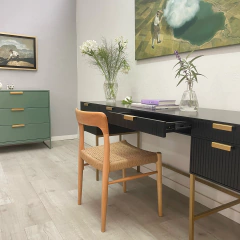 Vista de un escritorio moderno con una silla de madera, decorado con flores y libros, en un ambiente minimalista.