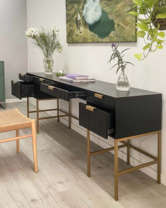 Un mueble negro moderno con cajones en un ambiente minimalista, decorado con flores y un cuadro en la pared.
