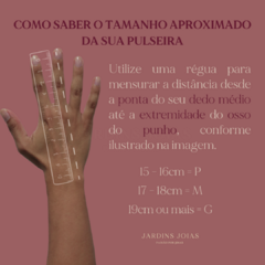 Uma mão segurando uma régua, mostrando como medir o tamanho de uma pulseira, com instruções sobre as medidas em centímetros.