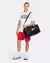 Homem vestindo camiseta branca e shorts vermelhos segurando bolsa preta Nike BRSLA S Duff 41L com alça de ombro