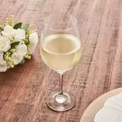 Copa Prestige de degustación de 600ml con vino blanco sobre una mesa de madera, junto a un ramo de flores blancas.