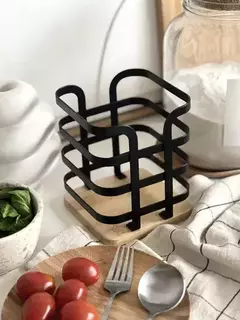 Soporte metálico para cubiertos con diseño moderno, ubicado en una mesa con frutas y utensilios de cocina.