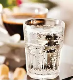 Vaso Bristol chico de 200 ml con agua con burbujas, en primer plano, con un fondo desenfocado de café.