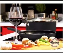 Juego de cacerolas antiadherentes HUDSON en una cocina moderna, acompañado de una copa de vino y verduras frescas.