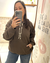 Mujer mostrando un buzo Mariela color chocolate con capucha y bolsillo canguro, tomando una selfie frente a un espejo