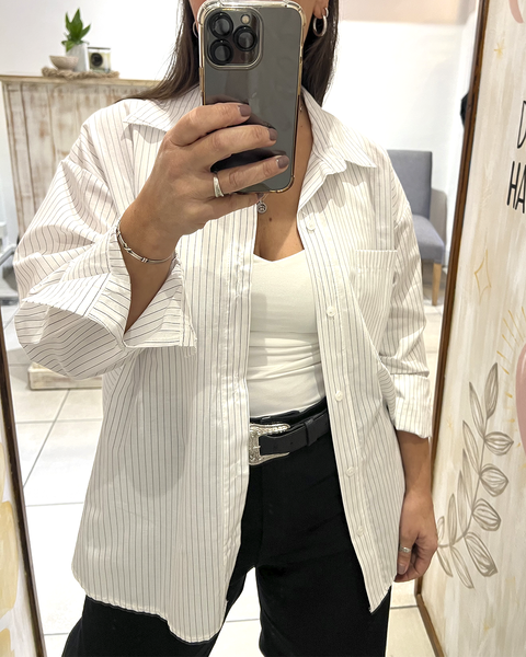 Mujer posando frente a un espejo la Camisa Lorena blanca de poplin rayado, con manga larga, bolsillo en el pecho y corte más largo atrás