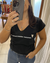 Remera negra con escote en V que dice "Las casualidades insisten" en la parte frontal.