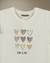 Remera Lara color offwhite de algodón con estampa de corazones en tonos tierra y detalles en foil, vista de frente sobre fondo beige.
