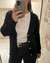 Mujer usando saco tejido color negro con botones simil madera y escote en V, con detalles calados.
