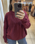 Mujer usando un sweater Benson de color bordó con diseño de trenzas, combinado con jeans azules.