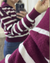 Mujer modelando el sweater Cora en color bordó con rayas blancas, haciendo foco en el puño de la manga.