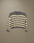 Sweater Iguazú color gris con crudo colgado sobre fondo beige, vista frontal.