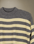 Sweater Iguazú color gris con crudo colgado sobre fondo beige, vista frontal.