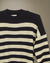Sweater Iguazú color negro con crudo colgado sobre fondo beige, vista frontal.