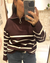Mujer usando un sweater Italy de color chocolate con rayas blancas y cuello alto con cierre.