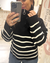 Mujer usando un sweater Italy de color negro con rayas blancas y cuello alto con cierre.