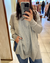Persona usando un sweater gris claro de manga larga con puños acanalados y jeans azules, sacándose una foto frente al espejo en una tienda de ropa.