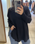 Persona usando un sweater negro de manga larga con puños acanalados y jeans azules, sacándose una foto frente al espejo en una tienda de ropa.