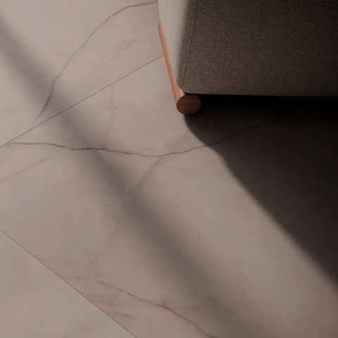 Piso de porcelanato acetinado 120x120 cm, com veios sutis, exibindo a esquina de um sofá com pés de madeira.