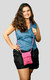 Modelo sorridente usando uma mini bolsa de crochê rosa, combinando com uma blusa azul e shorts pretos.