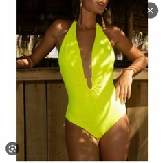 Mulher usando um maiô amarelo neon com recortes, posando em um ambiente tropical.