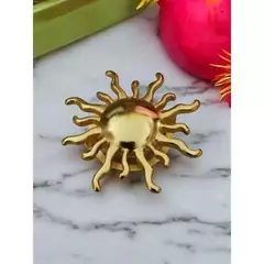 Fivela dourada em formato de sol para biquíni, ideal para vestidos, sobre fundo de mármore.